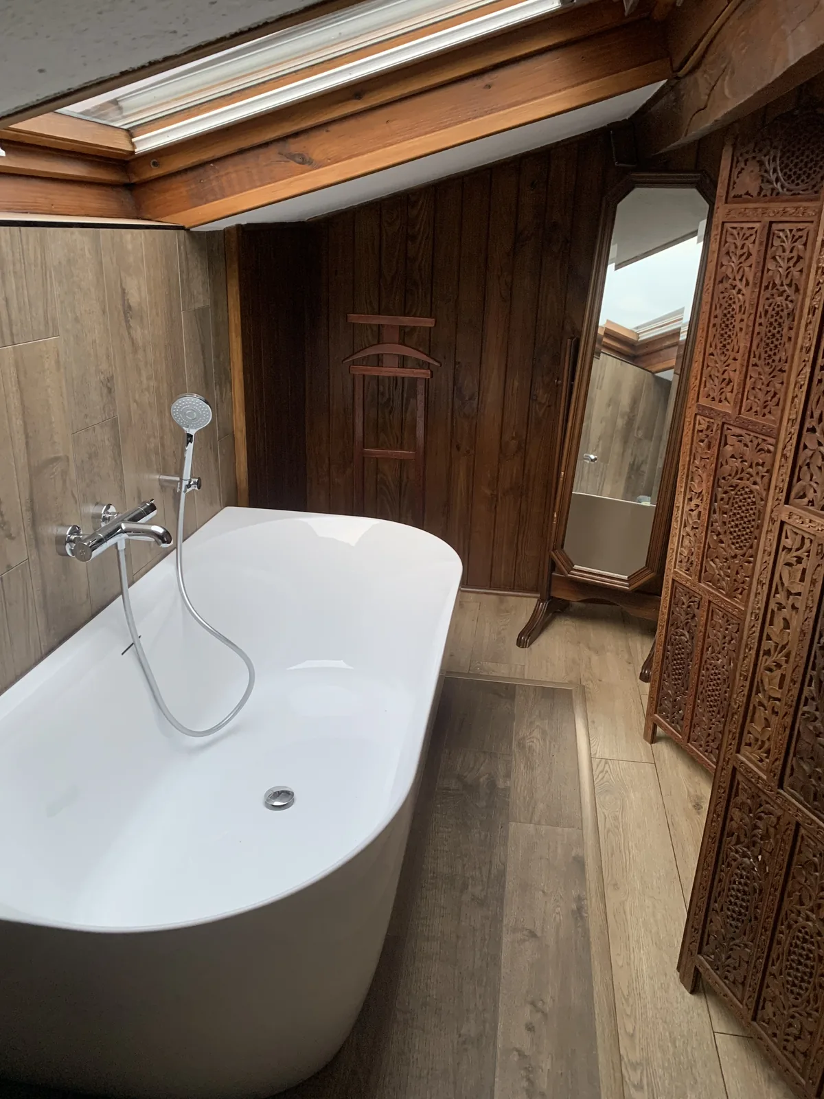 Salle de bains sous pente avec baignoire îlot et habillage bois